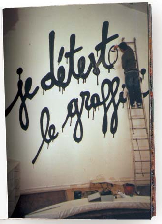 Chico subido a una escalera pintando un graffitti en una pared con el texto Je d'etesto le graffitti